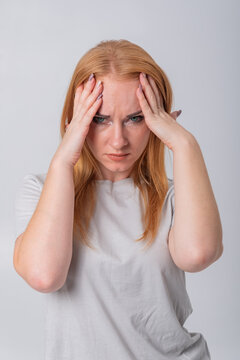 Young red haired woman with green eyes clutching her temples in pain, showing migraine related stress and frustration, tense expression conveying illness, discomfort and worry