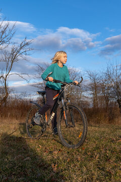 Blond boy actively riding a bicycle through a grassy field, looking away while enjoying the natural outdoor environment under a blue sky, symbolizing healthy lifestyle and childhood adventure