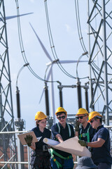 Fototapeta premium A commissioning team in navy suits and yellow hard hats check disconnector positions against the diagram inside the wind farm grid substation in crisp blue sky daylight at an operating.
