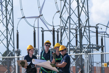 Fototapeta premium A commissioning team in navy suits and yellow hard hats check disconnector positions against the diagram inside the wind farm grid substation in crisp blue sky daylight deep inside a.