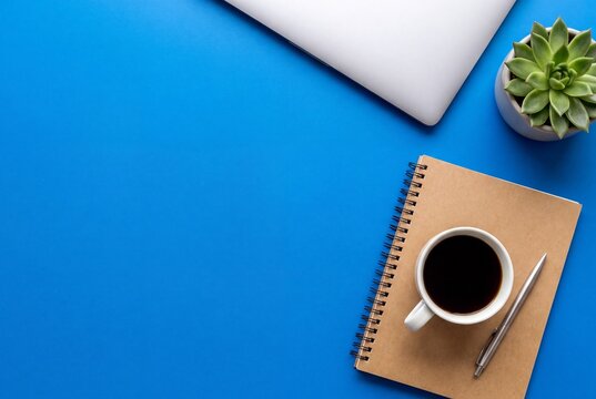 Top view of a workspace with a laptop, a notebook, a cup of black coffee, a pen, and a succulent plant on a blue background