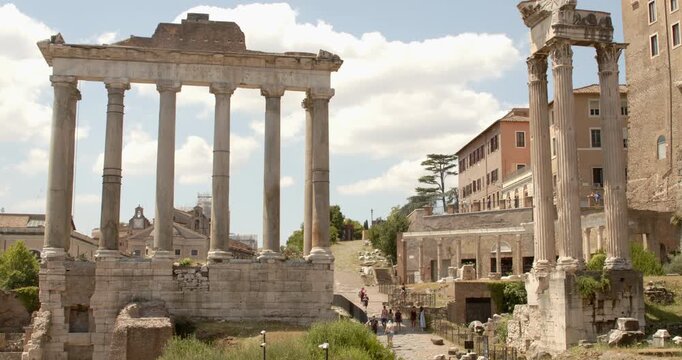 The majestic remaining columns of the Temple of Saturn stand prominently in the Roman Forum, showcasing a classic stone architrave supported by towering pillars against a summer sky in Rome, Italy.