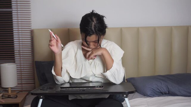 Teenage girl using tablet on bed at night while stressed thinking. Asian student hold stylus pen to study online inside bedroom during Gen Z lifestyle homework exam preparation.