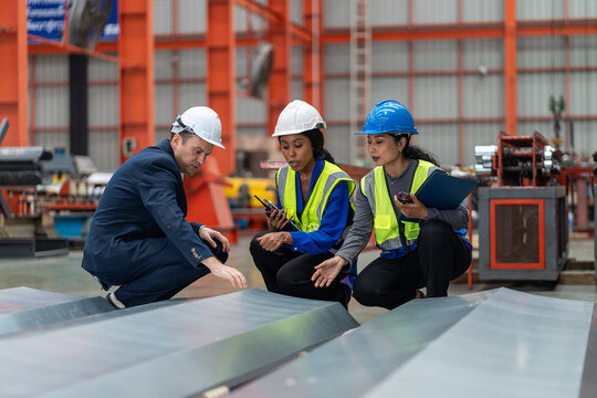 multiethnic group of industrial engineers and inspector wearing safety vests and hard hats working together in a manufacturing facility