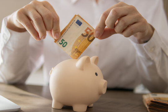 Person saving money by depositing fifty euro bank notes into a ceramic piggy bank, symbolizing financial investment, future planning, and personal budget management