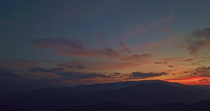 
Aerial Twilight Over the hill. This panoramic aerial photograph captures a vast mountain range at sunset. The sky is ablaze with warm pink and golden tones, casting a soft glow over the rugged peaks.