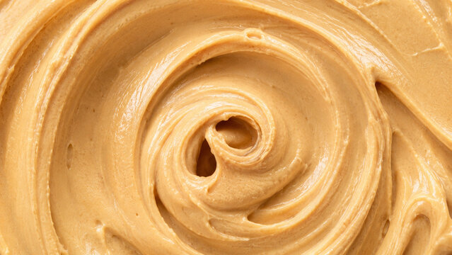 Creamy peanut butter swirl texture with smooth glossy surface in a macro food background.