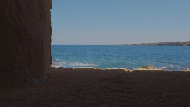 through an ancient stone archway, the blue sea of Sicily with the sound of its waves