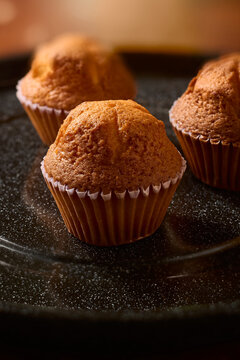 freshly baked golden muffins on dark speckled tray close-up, warm sweet pastry in paper cups, side view with soft focus and copy space, homemade dessert
