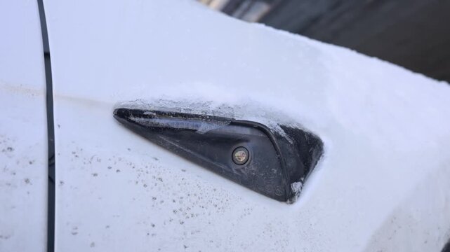 Detailed close up of a frozen car side camera lens surrounded by ice on a white fender. Extreme winter weather conditions can impact the performance of autonomous driving sensors.