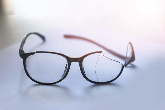 Closeup of Broken Eyeglasses with Cracked Lens on White Surface