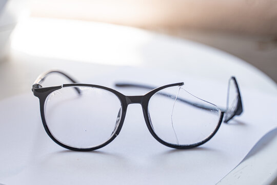 Closeup of Broken Eyeglasses with Cracked Lens on White Surface
