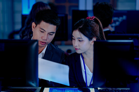 Diverse tech professionals collaborating intensely. Focused team synergy, reviewing project data side-by-side in a modern, blue-lit command center workspace.
