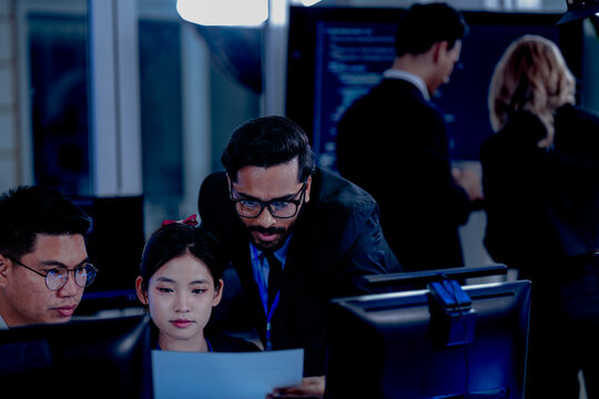 Critical AI model review. Senior data scientist leans over analyzing code output with junior engineers. Debugging complex algorithms together for optimal service performance at night.