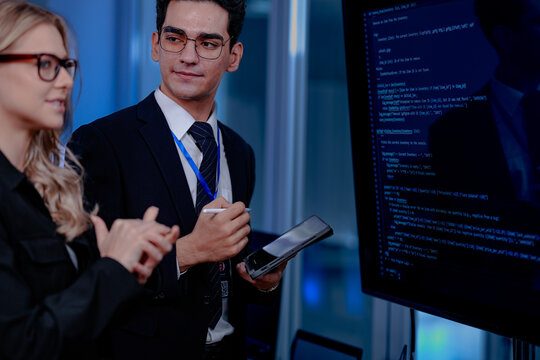 Code breakthrough achieved. Smiling senior developer points to a successful code segment on screen, sharing the solution with his colleague during a late night pair programming session.