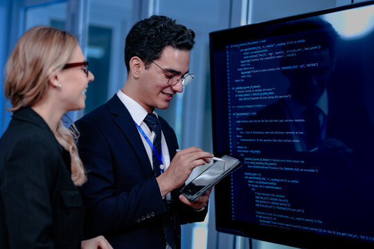 Intense code walkthrough. A female developer uses a stylus pointing to a specific line of code on the screen explaining its function to her male teammate during a debugging session.