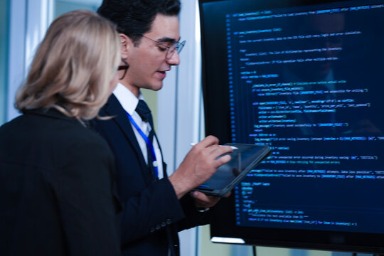 Monitoring AI training progress. Specialists oversee a machine learning model's training observing real time metrics on screen discussing adjustments via tablet interface late night.