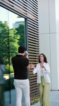 Young man taking pictures of an expressive woman posing outdoors in front of a modern building