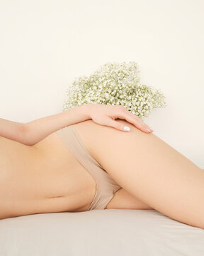 Close up of a woman in seamless nude panties holding a gypsophila bouquet against her hip. Perfect for lingerie brands, laser hair removal clinics, and body care advertising.
