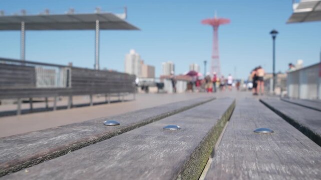 Coney Island beach, wooden pier promenade in Brooklyn, New York, United States. Boardwalk near retro luna park. Amusement park on ocean coast beach. People on waterfront summer holiday in NYC, USA.