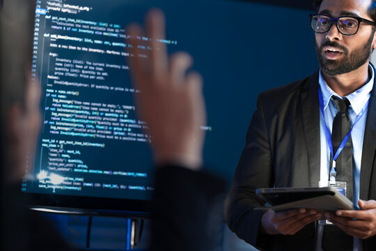 An Indian male software engineer or team lead discusses Python code for an AI algorithm. A developer in the audience raises their hand to ask a technical question during a code review.