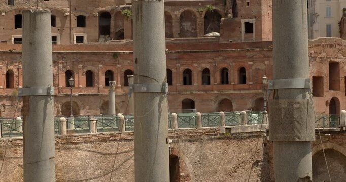 A closeup view of the Trajan's Forum archaeological site in Rome, Italy, displaying weathered granite columns standing among ancient stone fragments, brick structures, and historical buildings.
