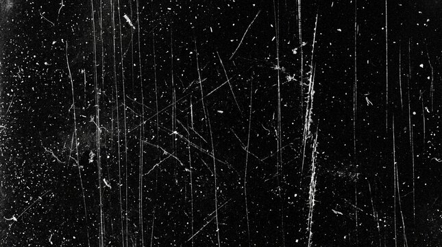 Closeup of scratched black surface with white specks and lines, textured background