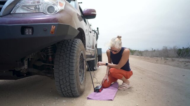 A senior woman smiles while airing up tires on her suv and teardrop camper after a desert camping trip in Baja California, Mexico.
