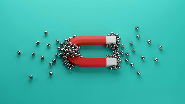 Red horseshoe magnet attracting scattered metal spheres on teal background