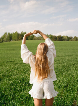 Woman stretches arms in green field on sunny day