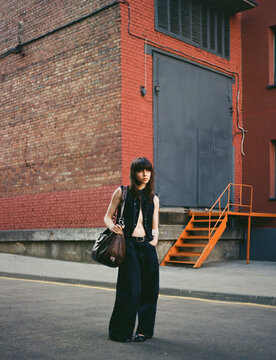 Young person stands casually on city street near brick building