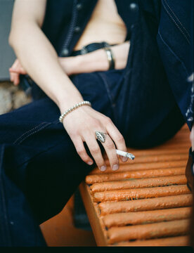Young person sits on a bench holding a cigarette