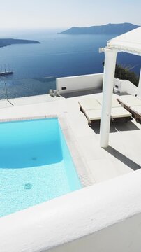 White architecture in Santorini island, Greece. Luxury swimming pool with blue water. Blue sea and the blue sky at sunny day. Travel and summer vacation concept. Vertical video
