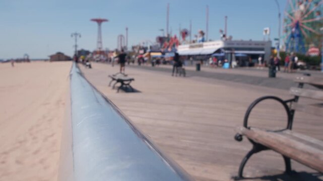 Coney Island beach promenade in Brooklyn, New York, United States. Wooden boardwalk near retro luna park. Amusement park on ocean coast beach. Waterfront summer holiday, people walking on promenade.