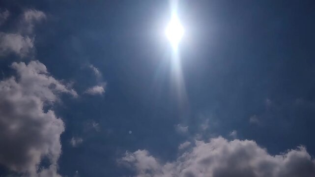 Low angle wide shot of the bright sun creating intense lens flares while white clouds drift by.