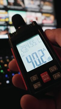 A person holds a digital decibel meter displaying forty decibels while measuring the noise of a working laptop. The illuminated RGB keyboard and screen glow softly in the dark room.