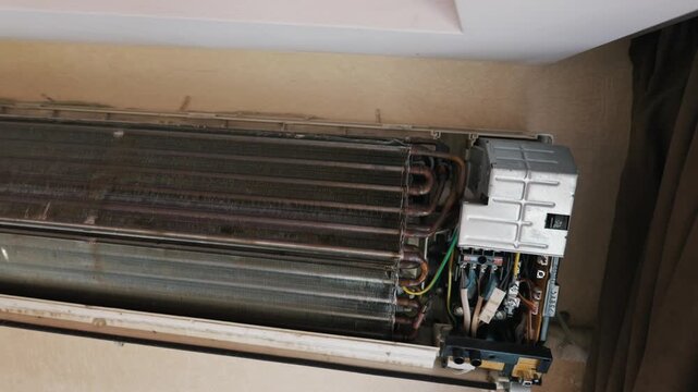 An opened wall air conditioner unit exposes a dirty radiator and copper tubes. The internal cooling fins are covered in dangerous mold and dust buildup. Maintenance is urgently needed.