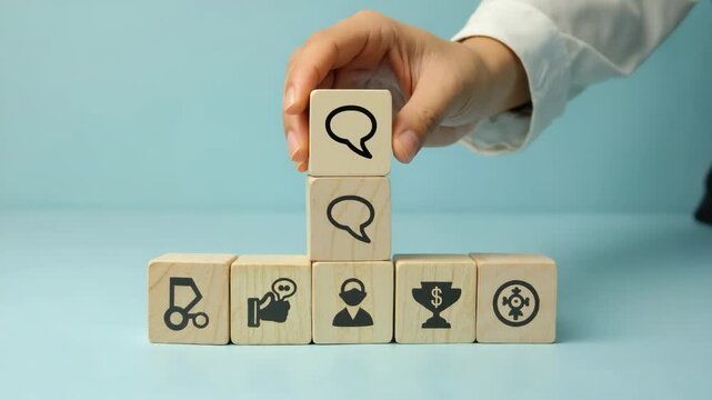 A hand stacks wooden blocks with business icons, representing teamwork, communication, management, and leadership in a corporate environment. Suitable for presentations and articles. Doodle symbols