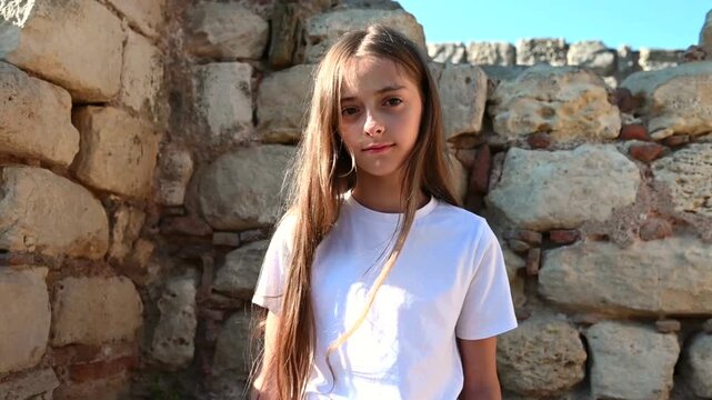 Young girl sitting near an ancient stone wall in warm natural sunlight. Ideal for themes of childhood, travel, history, culture, and summer lifestyle.