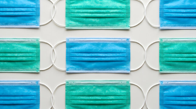 Blue and green surgical masks arranged neatly in a repeating pattern on white background