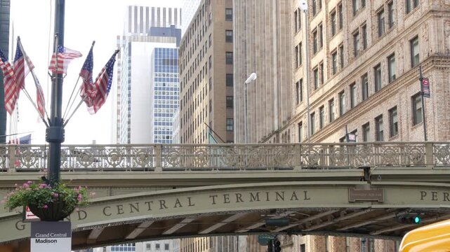American flags near Grand Central Terminal on 42 street, New York City, Manhattan Midtown. Bridge to railway building, urban architecture in United States. Public railroad transport junction.