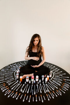 Pregnant woman surrounded by fertility needles and syringes