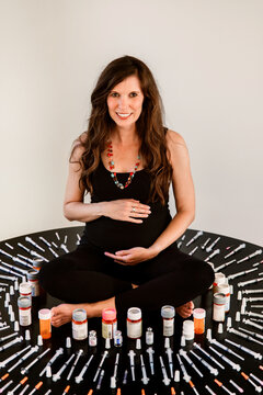 Pregnant woman surrounded by IVF syringes and medicine bottles
