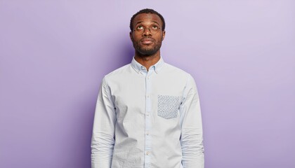 Obraz premium Contemplative african american man looks thoughtfully upwards against soft lavender background