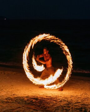 Man performing fire dance on a sandy beach at night creating a fiery circle