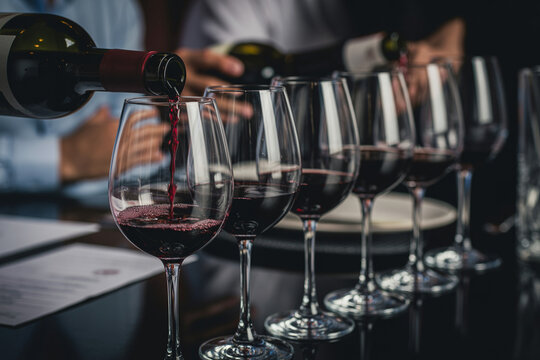 Professional waiter pouring red wine into crystal glasses for tasting event in restaurant or luxury dining setting.