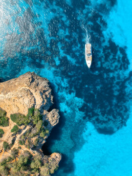 Aerial view of luxury motor boat yacht in turquoise sea water in Mallorca, Balearic island, Spain. Speedboat moving near rocky cliff coast. Drone summer landscape. Cruise. Top down view. Travel
