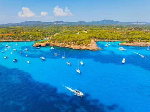 Aerial drone view of yachts and boats in a sea bay in Mallorca, Spain. Summer vacation, leisure and recreation near the Mediterranean coastal forest.
