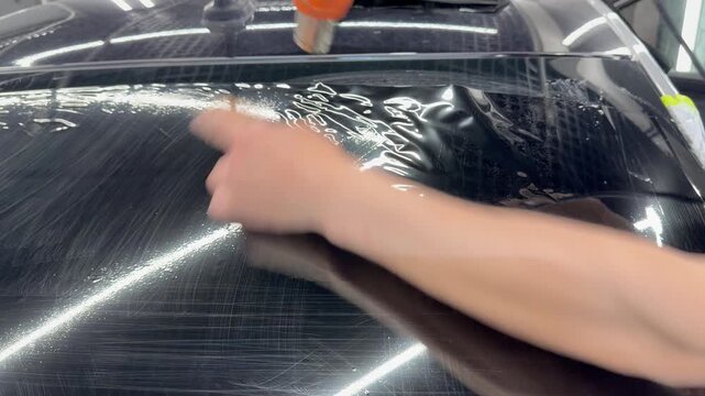 Professional car window tinting process: technician prepares the glass, applies tint film, uses a heat gun to shape it on curved surfaces, and smooths out air bubbles with a squeegee. 