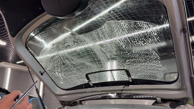 Professional car window tinting process: technician prepares the glass, applies tint film, uses a heat gun to shape it on curved surfaces, and smooths out air bubbles with a squeegee. 